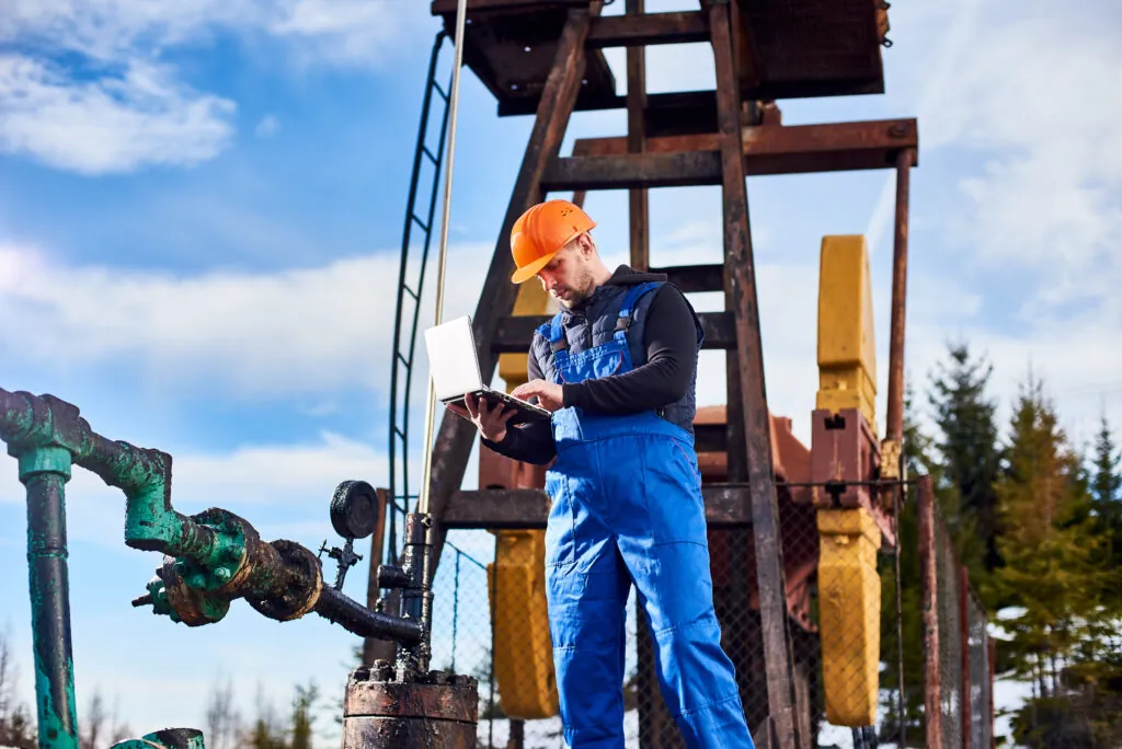 An engineer using laptop in an Oil field near machinery & equipment.